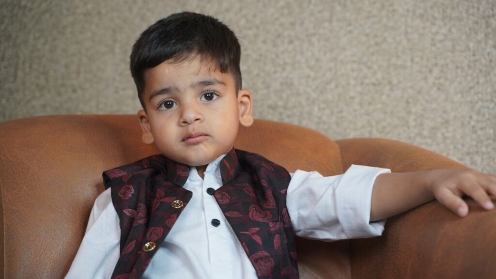 A young child in traditional clothing sitting on a couch, looking contemplative.