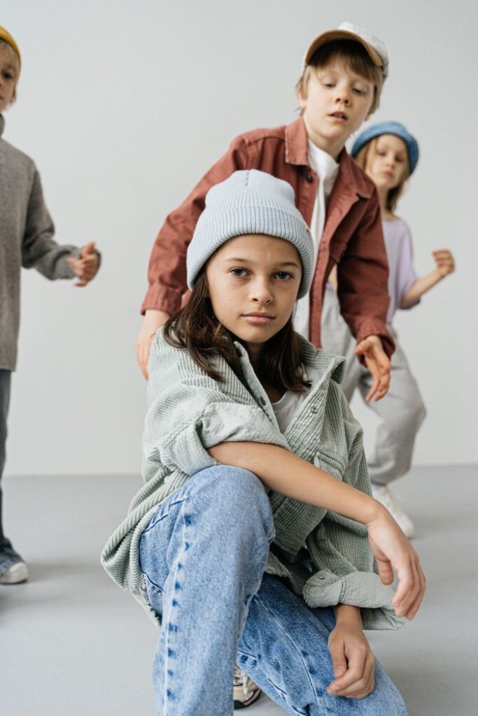 Four children in fashionable jackets and caps posing creatively against a white background.